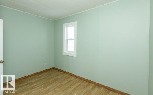 Room featuring light green walls, wood-finish flooring, a white trim window, and white door with brass hardware - 9836 100 Street, Westlock, AB 