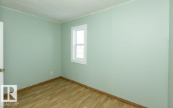 Room featuring light green walls, wood-finish flooring, a white trim window, and white door with brass hardware - 