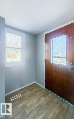 Entryway featuring a wood-panel door with privacy glass, wood-finish flooring, light gray walls, white trim, and a window providing natural illumination - 9836 100 Street, Westlock, AB 