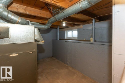 Utility room featuring a forced-air furnace with associated ductwork, painted cinder block walls, exposed wood ceiling joists, and a small basement window - 9836 100 Street, Westlock, AB 