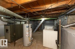 Utility space featuring exposed ceiling joists, a water heater, a furnace system, and foundational walls - 