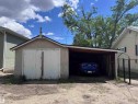 Detached single-car garage featuring a stucco exterior and a side carport with a wood-finish ceiling - 9836 100 Street, Westlock, AB 