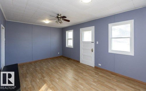 Bright interior space featuring wood-finish flooring, a ceiling fan with integrated lighting, and two windows providing natural illumination - 9836 100 Street, Westlock, AB 