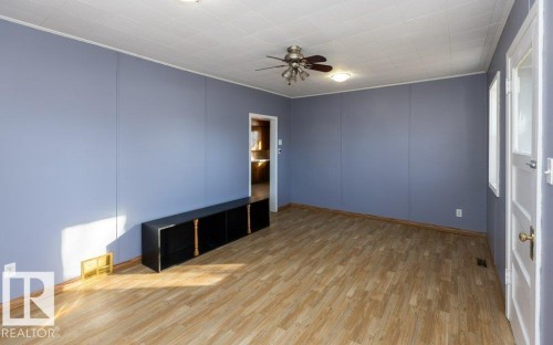 Spacious room featuring light wood-finish flooring, a ceiling fan with integrated lighting, and a white paneled door with glass inserts - 9836 100 Street, Westlock, AB 