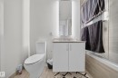 Contemporary bathroom featuring a white vanity with a light-toned countertop, an illuminated mirrored medicine cabinet, a modern toilet, and a bathtub with a tiled surround - 4007 10360 102 Street, Edmonton, AB 