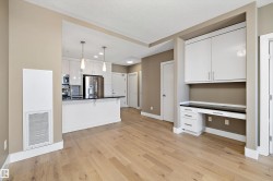 Light wood-finish flooring extending into an open-concept kitchen featuring white cabinetry, a dark countertop, and stainless steel appliances - 