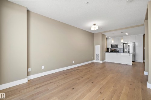Open-concept living area with wood-finish flooring, a contemporary ceiling light fixture, and neutral wall tones - 307 11080 Ellerslie Rd Sw, Edmonton, AB 
