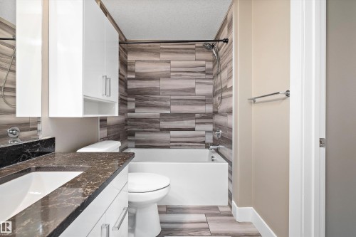Bathroom featuring a white vanity with a dark stone-finish countertop, undermount sink, and chrome fixtures - 307 11080 Ellerslie Rd Sw, Edmonton, AB 
