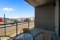 Private west facing balcony featuring concrete flooring and a glass panel railing system with black metal supports. - 