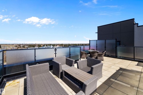 The expansive north rooftop patio featuring large format tile flooring, black metal railing with frosted glass panels, and a surrounding privacy screen, gives a view of Downtown Edmonton. - 307 11080 Ellerslie Rd Sw, Edmonton, AB 
