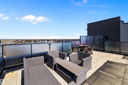 The expansive north rooftop patio featuring large format tile flooring, black metal railing with frosted glass panels, and a surrounding privacy screen, gives a view of Downtown Edmonton. - 