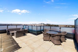 The expansive north rooftop patio featuring large format tile flooring, black metal railing with frosted glass panels, and a surrounding privacy screen, gives a view of Downtown Edmonton. - 