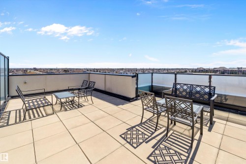 The expansive south rooftop patio featuring large format tile flooring, black metal railing with frosted glass panels, and a surrounding privacy screen, gives an opportunity for a lot of sun and sunsets. - 307 11080 Ellerslie Rd Sw, Edmonton, AB 