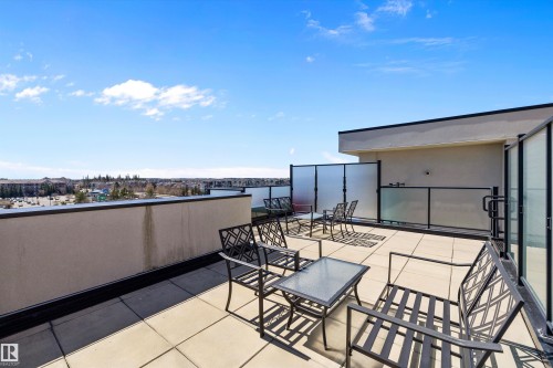 The expansive south rooftop patio featuring large format tile flooring, black metal railing with frosted glass panels, and a surrounding privacy screen, gives an opportunity for a lot of sun and sunsets. - 307 11080 Ellerslie Rd Sw, Edmonton, AB 