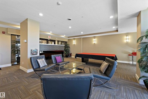 The Recreation Room has a modern kitchen featuring a striking red island countertop, stainless steel appliances, dark wood-finish cabinetry, and a dark subway tile backsplash, with a pool table and a lounge type seating to enjoy with your company. - 307 11080 Ellerslie Rd Sw, Edmonton, AB 