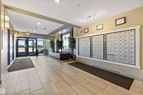 Building entrance foyer featuring tile flooring and an integrated mailbox system. - 307 11080 Ellerslie Rd Sw, Edmonton, AB 