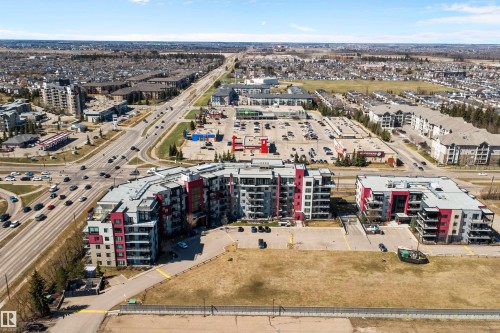 Modern multi-story residential buildings featuring contemporary architecture with vibrant red and gray facade panels. - 307 11080 Ellerslie Rd Sw, Edmonton, AB 