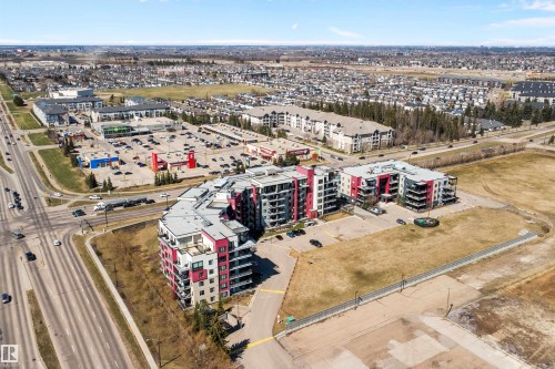 Modern multi-story residential buildings featuring contemporary architecture with vibrant red and gray facade panels. - 307 11080 Ellerslie Rd Sw, Edmonton, AB 