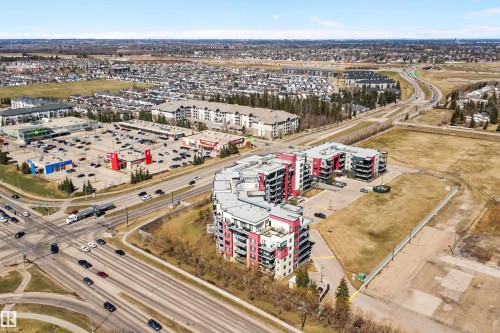 Modern multi-story residential buildings featuring contemporary architecture with vibrant red and gray facade panels. - 307 11080 Ellerslie Rd Sw, Edmonton, AB 