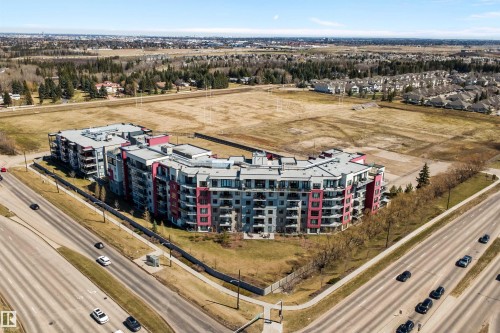 Modern multi-story residential buildings featuring contemporary architecture with vibrant red and gray facade panels. - 307 11080 Ellerslie Rd Sw, Edmonton, AB 