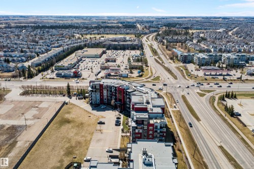 Modern multi-story residential buildings featuring contemporary architecture with vibrant red and gray facade panels. - 307 11080 Ellerslie Rd Sw, Edmonton, AB 