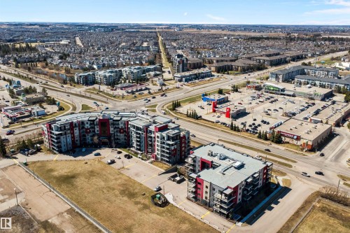Modern multi-story residential buildings featuring contemporary architecture with vibrant red and gray facade panels. - 307 11080 Ellerslie Rd Sw, Edmonton, AB 