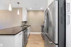 Modern kitchen featuring a large island with a dark quartz countertop, white cabinetry, stainless steel appliances, and wood-finish flooring. - 