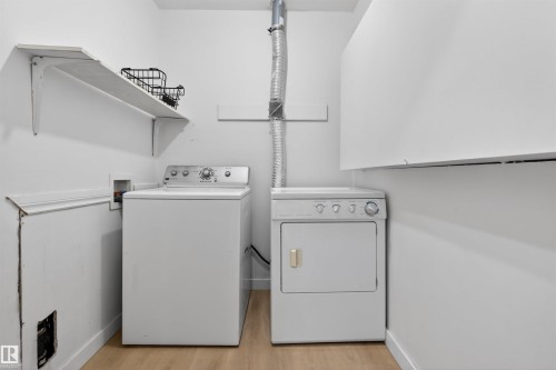 Dedicated laundry area featuring a white washing machine, white dryer, built-in upper cabinetry, and wall-mounted shelving - 7304/7306 78 Avenue, Edmonton, AB 