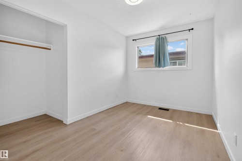 Bright interior room featuring wood-finish flooring, a double-hung window, and a built-in closet with shelving and a hanging rod - 7304/7306 78 Avenue, Edmonton, AB 