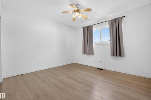 Spacious room featuring light wood-finish flooring, white walls, and a ceiling fan with integrated lighting - 7304/7306 78 Avenue, Edmonton, AB 