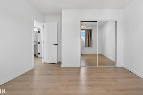Light wood-finish flooring complements crisp white walls in this room, featuring a mirrored closet with sliding doors and a six-panel door with matte black hardware - 7304/7306 78 Avenue, Edmonton, AB 