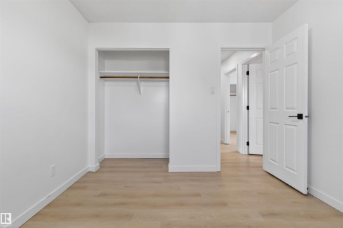 Room featuring light wood-finish flooring, white baseboards, and a closet with a built-in shelf and hanging rod - 7304/7306 78 Avenue, Edmonton, AB 