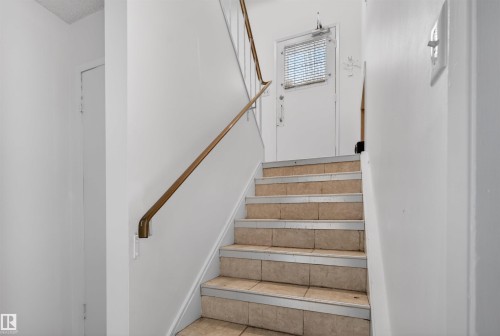 Tiled staircase featuring a metal handrail and white painted walls - 7304/7306 78 Avenue, Edmonton, AB 