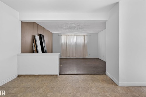 Interior space featuring distinct flooring areas: a light-toned tiled floor in the foreground and dark wood-finish flooring beyond a partial wall - 7304/7306 78 Avenue, Edmonton, AB 