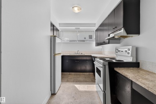 Galley kitchen featuring dark cabinetry, laminate countertops, a white electric range, and a white refrigerator - 7304/7306 78 Avenue, Edmonton, AB 