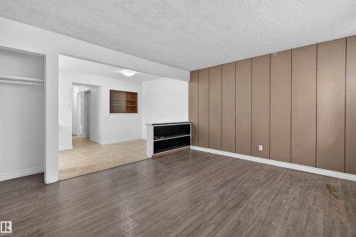 Open concept living area featuring wood-finish flooring, a full wall of vertical paneling, and an integrated built-in shelving unit - 7304/7306 78 Avenue, Edmonton, AB 