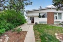 Single-story residence featuring white siding, a prominent brick accent wall, and a dark entry door - 7304/7306 78 Avenue, Edmonton, AB 