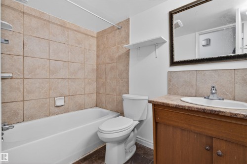 Bathroom featuring a porcelain bathtub, tile surround, wood-finish vanity, integrated sink, and an ornate framed mirror - 7304/7306 78 Avenue, Edmonton, AB 