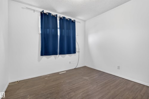 Room featuring wood-finish flooring, white baseboards, and a window with blue curtains - 7304/7306 78 Avenue, Edmonton, AB 