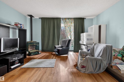 Living area featuring wood-finish flooring, light blue wall paint, and a corner-installed freestanding fireplace with a dark metal flue - 7304/7306 78 Avenue, Edmonton, AB 
