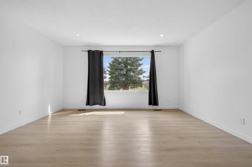 Spacious room featuring light wood-finish flooring, recessed lighting, and a large window with exterior tree views - 7304/7306 78 Avenue, Edmonton, AB 