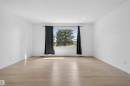 Spacious room featuring light wood-finish flooring, recessed lighting, and a large window with exterior tree views - 7304/7306 78 Avenue, Edmonton, AB 
