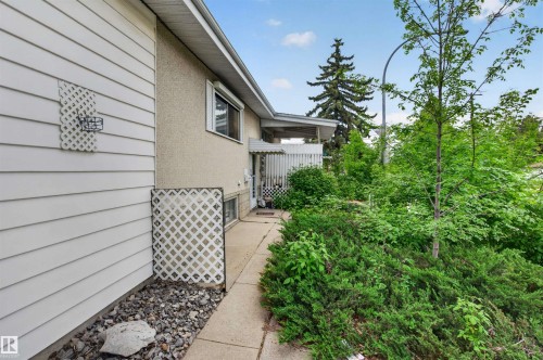 Exterior siding with decorative lattice details, paved walkway, covered entry, and lush perimeter landscaping - 7304/7306 78 Avenue, Edmonton, AB 