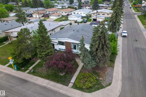 Corner lot property featuring a white exterior with brick accents, mature evergreen trees, and established landscaping - 7304/7306 78 Avenue, Edmonton, AB 