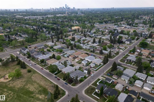 Aerial perspective showcasing residential streets with numerous detached homes, mature trees, and a distant city skyline - 7304/7306 78 Avenue, Edmonton, AB 