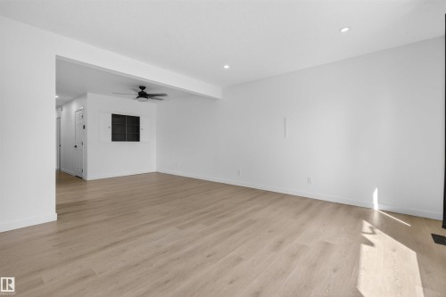 Spacious room featuring light wood-finish flooring, recessed lighting, and a modern ceiling fan - 7304/7306 78 Avenue, Edmonton, AB 