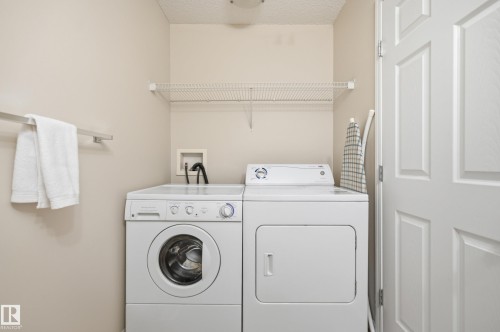 Dedicated laundry area featuring a white front-load washer and dryer set, neutral wall paint, and a white wire shelf for storage - 11628 167A Avenue, Edmonton, AB - Indoor Photo Showing Laundry Room