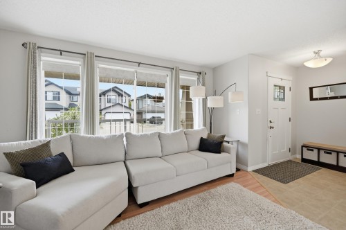 Living area featuring multiple large windows, wood-finish flooring, a front entry door with decorative glass, and tile flooring at the entry - 11628 167A Avenue, Edmonton, AB - Indoor Photo Showing Living Room