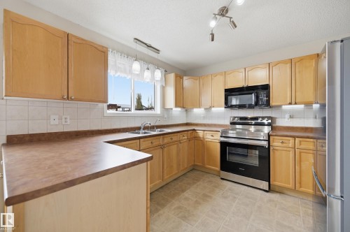 Kitchen featuring light wood cabinetry, a double basin sink, stainless steel range, built-in microwave, and track lighting - 11628 167A Avenue, Edmonton, AB - Indoor Photo Showing Kitchen With Stainless Steel Kitchen With Double Sink