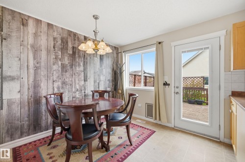 Dining area featuring a decorative wood-panel accent wall, a multi-light chandelier, a window, and a glass-paneled exterior door opening to a deck - 11628 167A Avenue, Edmonton, AB - Indoor Photo Showing Dining Room